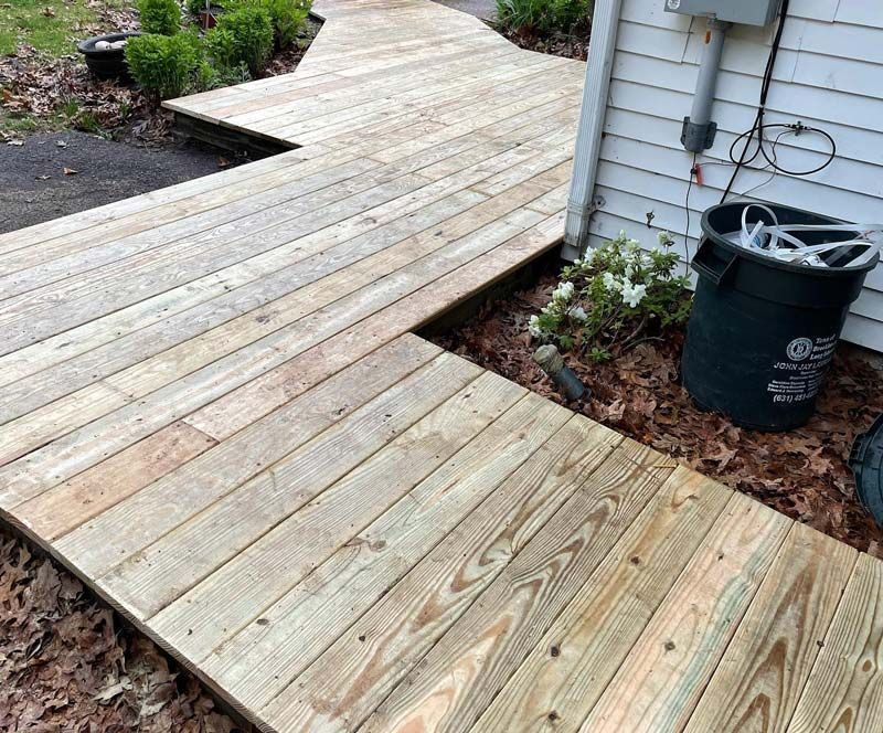 Wooden walkway leading past a house. The boards are weathered. A trash can sits beside the house.