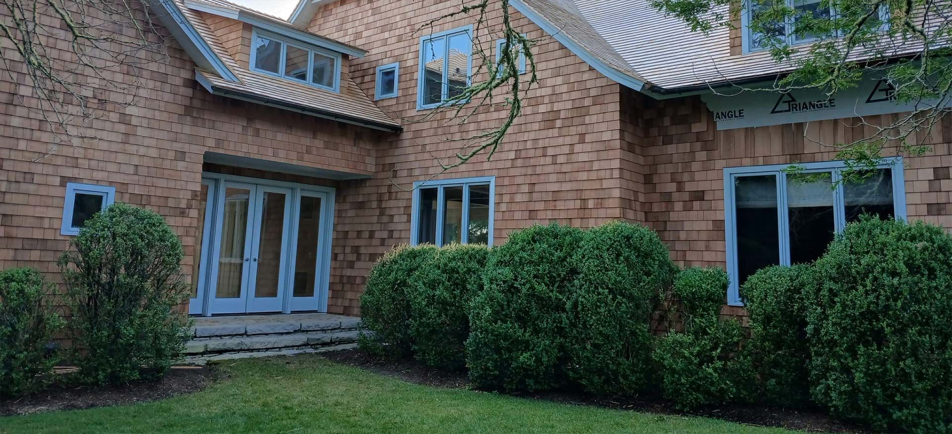 Brick house with light blue trim and windows, a white roof, and green bushes.