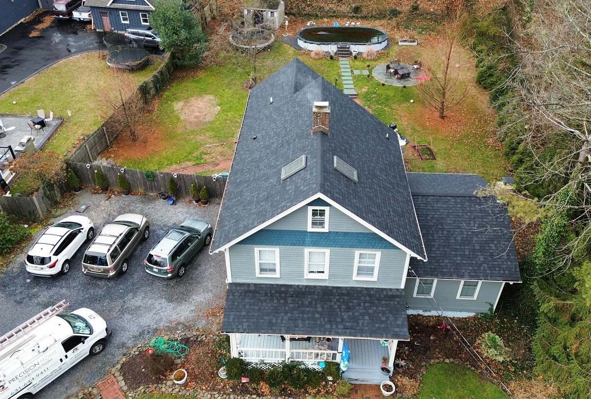 Aerial view of a two-story house with cars parked in the driveway and a pool in the backyard.