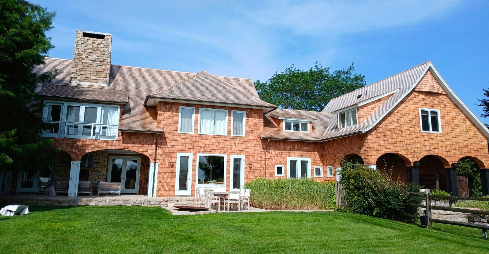 Large brick house with cedar shake roof, green lawn, blue sky.