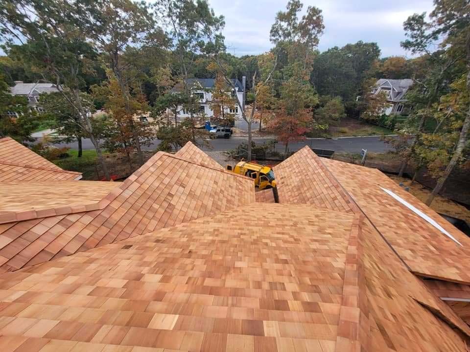 Wooden shingle roof under construction, aerial view of multiple sections with a road and trees in background.