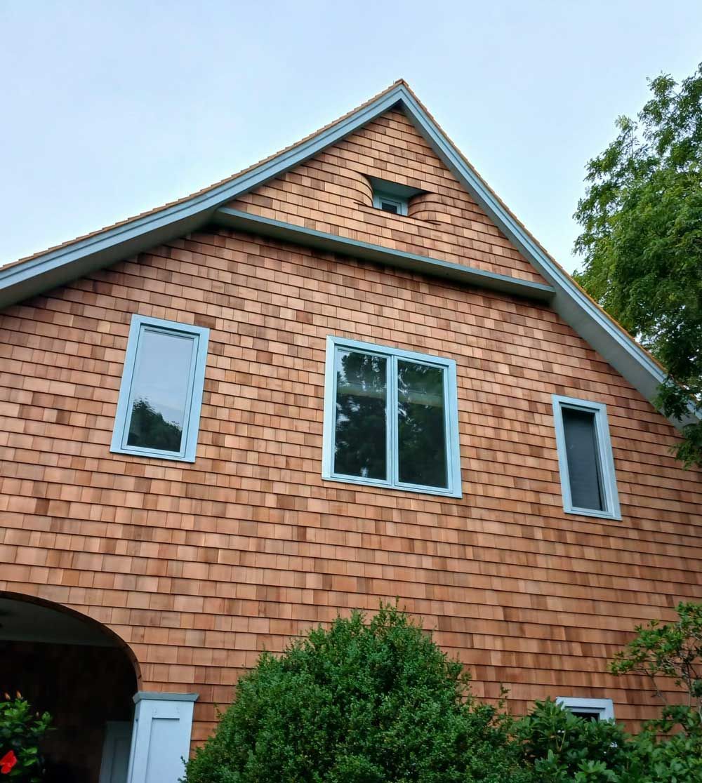 A house with a shingle facade, blue-trimmed windows, and a triangular roof with a star-shaped ornament.