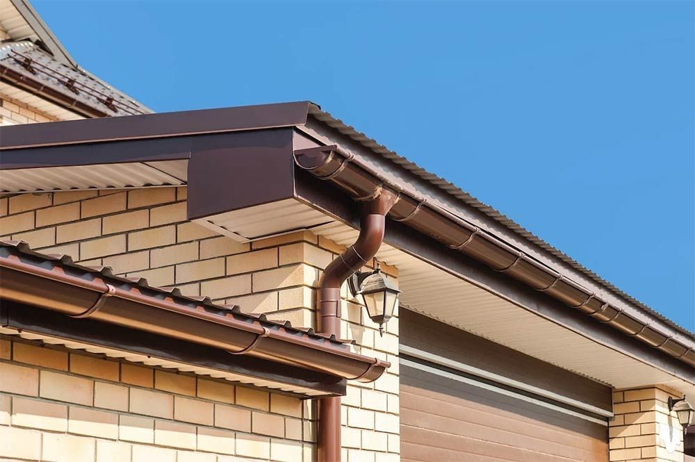 Brown gutters and downspouts on a brick building with a blue sky.
