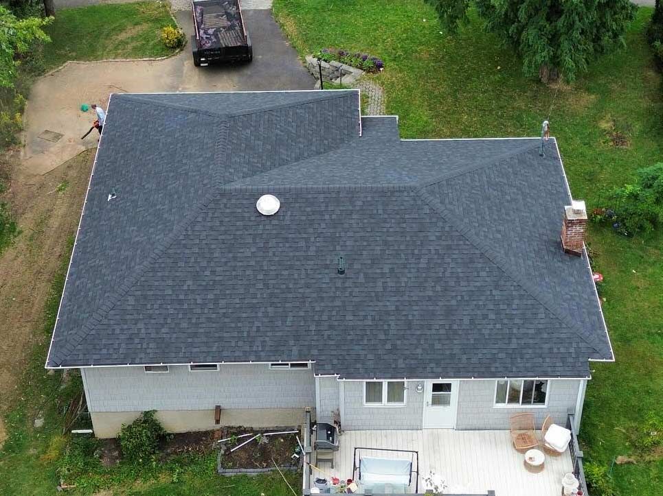 Overhead view of a house with a dark gray shingle roof, white siding, and a wooden deck.