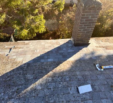 Rooftop with a brick chimney casting a long shadow, showing a caulking gun and debris.