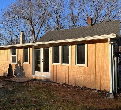 Exterior view of a building under construction with new wood siding, windows, and white trim.