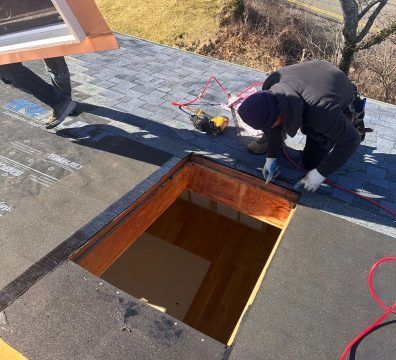 Two people installing a skylight on a rooftop. One worker is inside the open frame.
