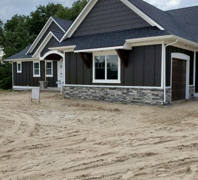 Brown-sided house with stone base, white trim, and a dirt yard.