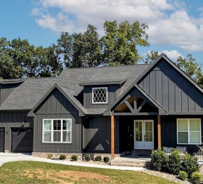 Dark gray house with white trim, a brown wooden porch, and a gray roof under a blue sky.