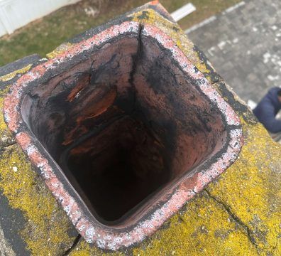 View down a square brick chimney showing soot, cracks, and moss on the exterior.