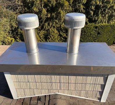 Two silver vents on a metal surface, atop a structure with gray shake siding.