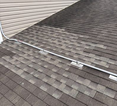 Gray roof with a metallic pipe secured by brackets near the siding of a building.