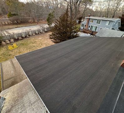 Flat, dark asphalt roof with a residential backyard and house in the background.
