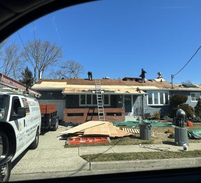 Roofers working on a residential roof on a sunny day. A truck and debris are in the foreground.