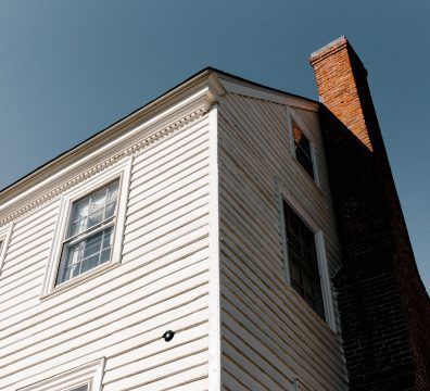 White house corner with brick chimney against blue sky.
