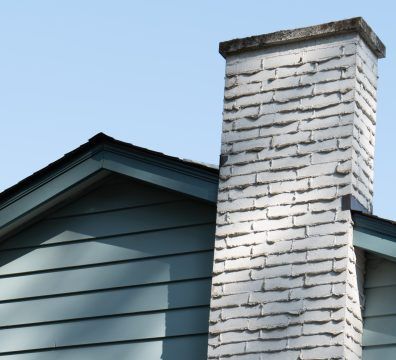 Blue house siding and chimney against a blue sky.