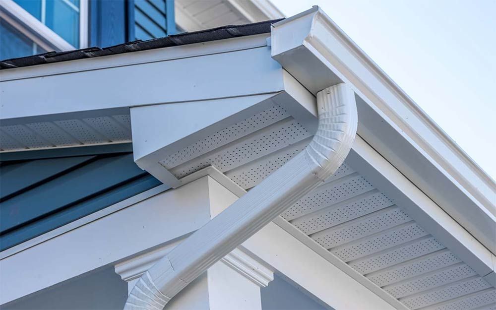 White gutters and downspout on a house with blue siding and a white trim.
