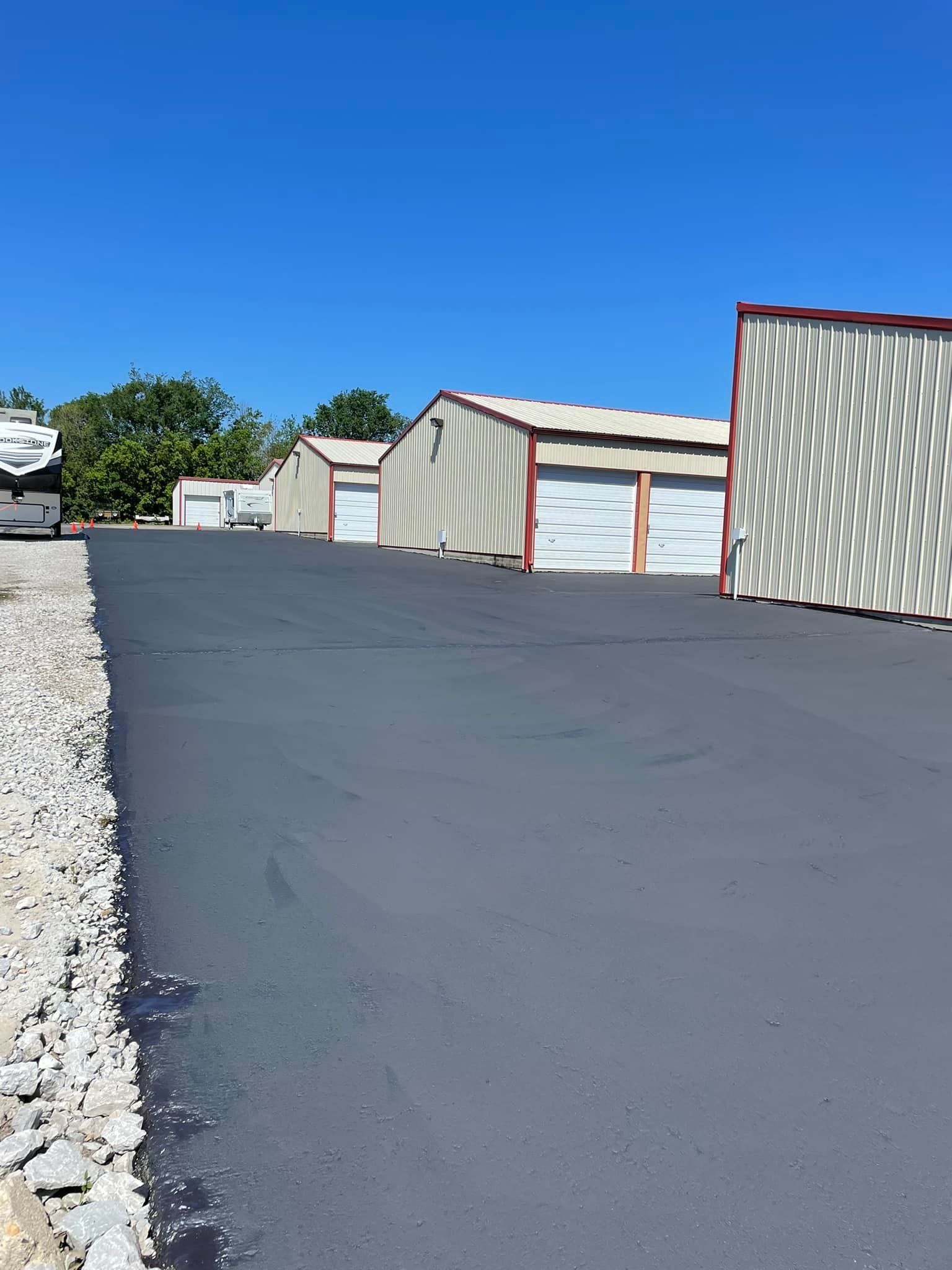 Rows of metal storage units with white doors, black asphalt driveway under a blue sky.