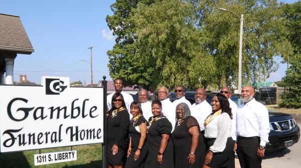 Group posing outside Gamble Funeral Home sign on a sunny day