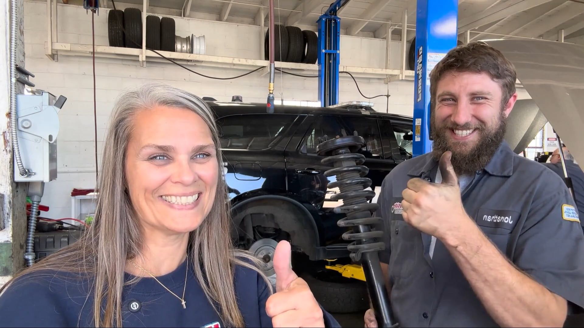Wayside Garage team members smiling in the shop, holding a strut and giving a thumbs up after a repair.