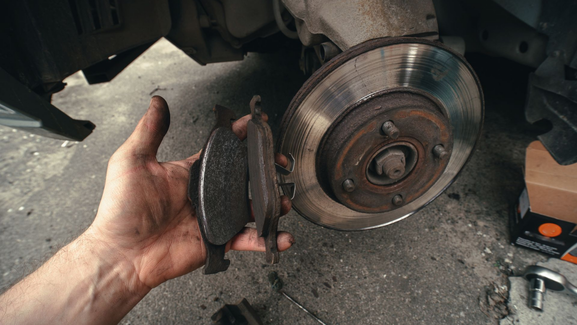 Mechanic holding a pair of worn brake pads next to a rusted brake rotor assembly during an inspection at Wayside Garage in Seaside CA