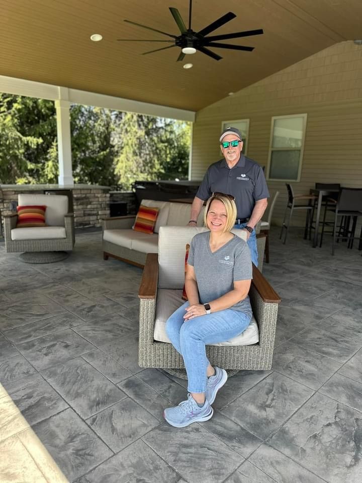 Two people seated on patio chairs under a covered outdoor area with a ceiling fan and lounge seating.