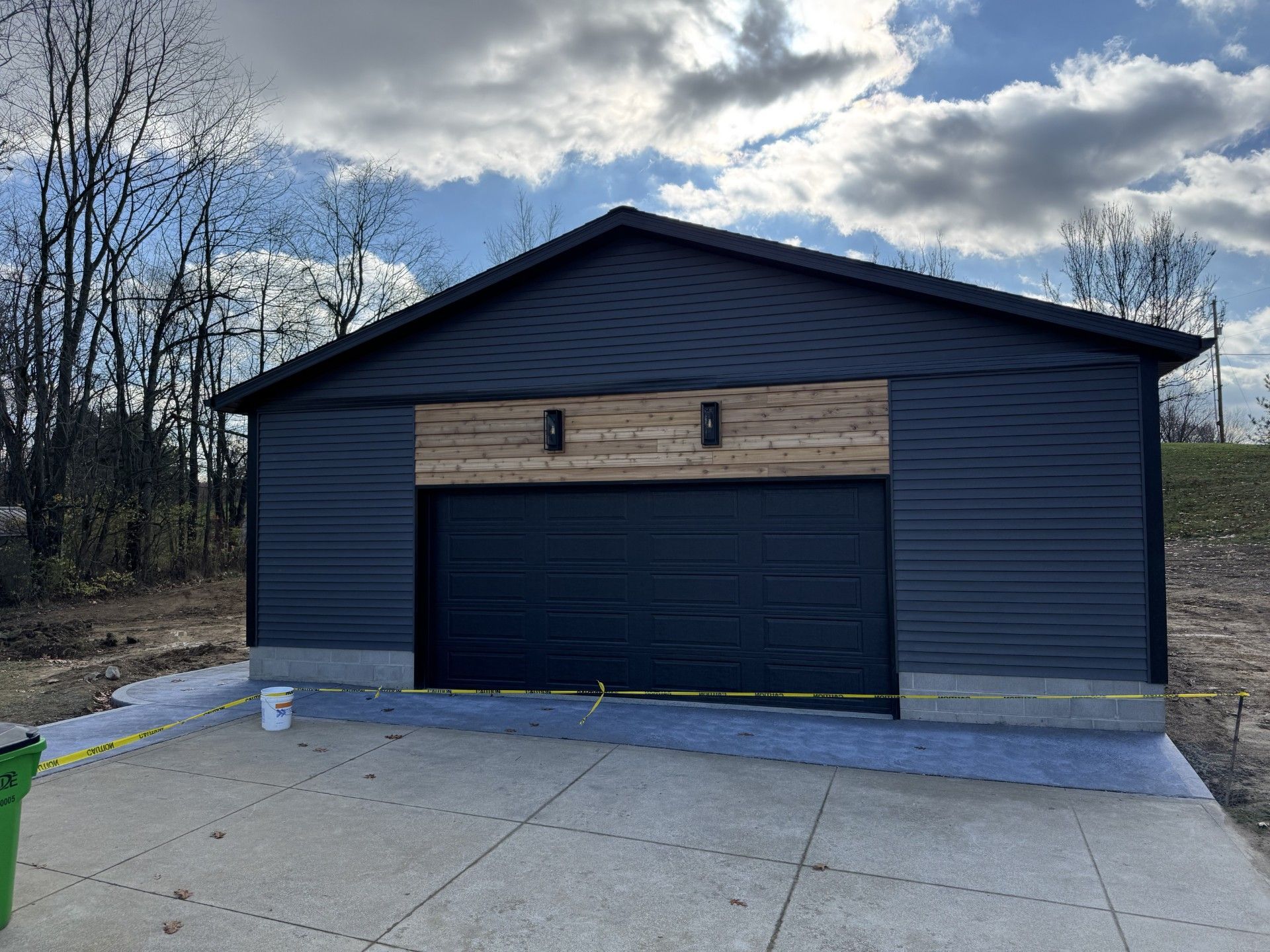 Blue garage with a large black door and concrete driveway under a cloudy sky.