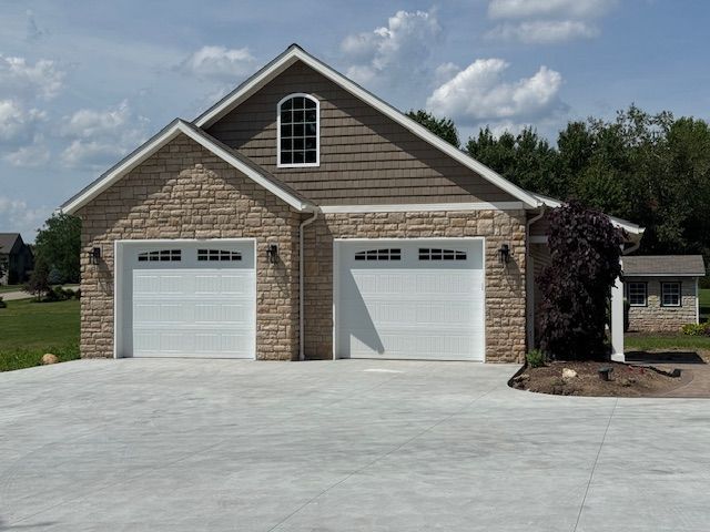 Two-car brick garage with white doors and a wide concrete driveway under a partly cloudy sky