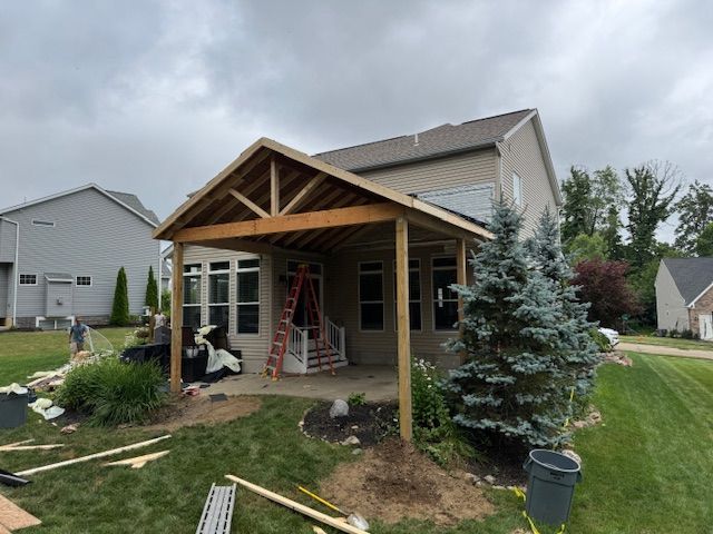 Partially built wooden porch with a red ladder in a suburban backyard under cloudy skies