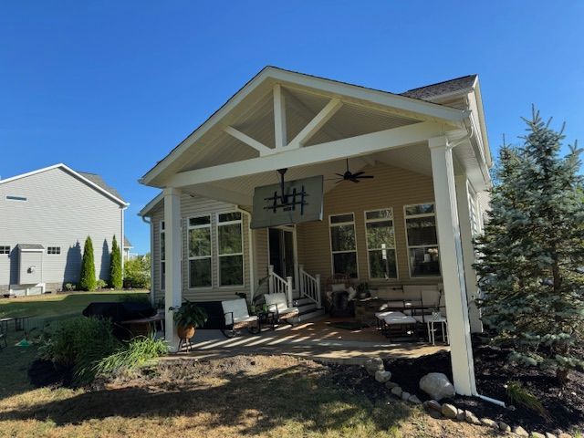 Front porch of a beige house with white beams, large windows, and a small seating area under a blue sky
