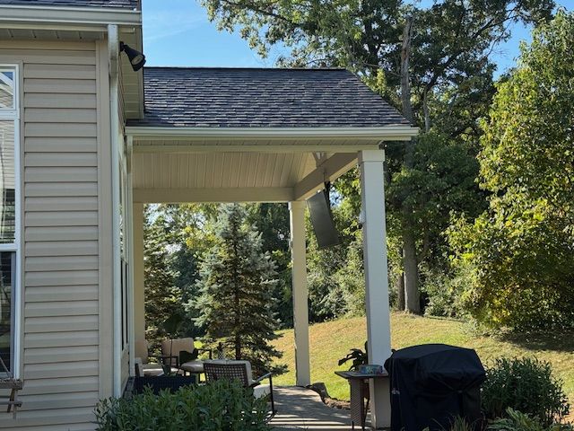 Side view of a house with a covered porch, white columns, and a backyard lawn with trees.