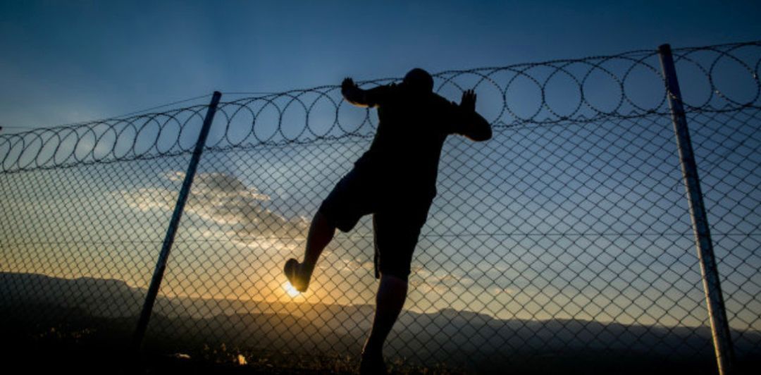 A man is jumping over a barbed wire fence at sunset.