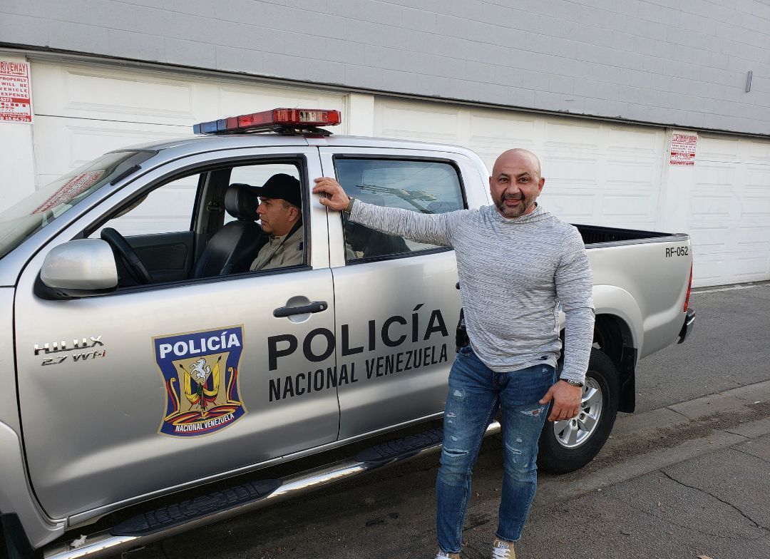 A man is standing in front of a silver police truck