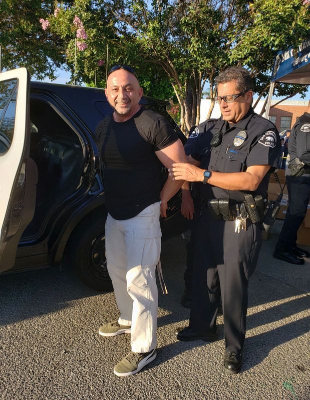 Man in handcuffs being arrested by a police officer near a police car.