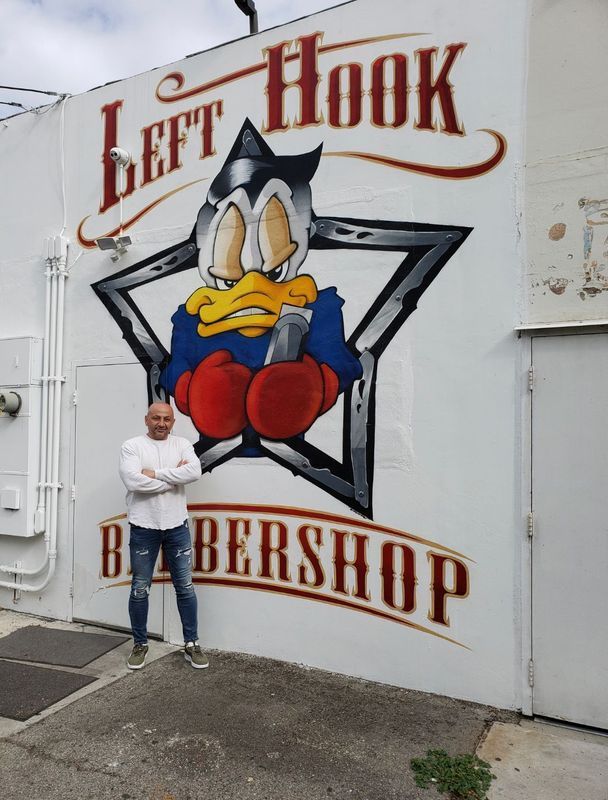 A man stands in front of a left hook barbershop mural