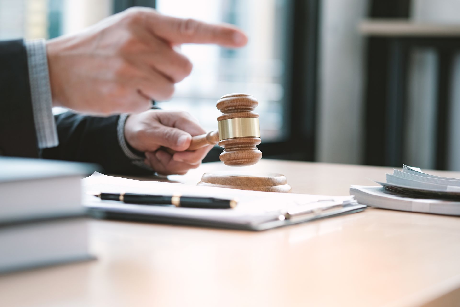 Hand holding gavel and pointing finger at documents on desk.