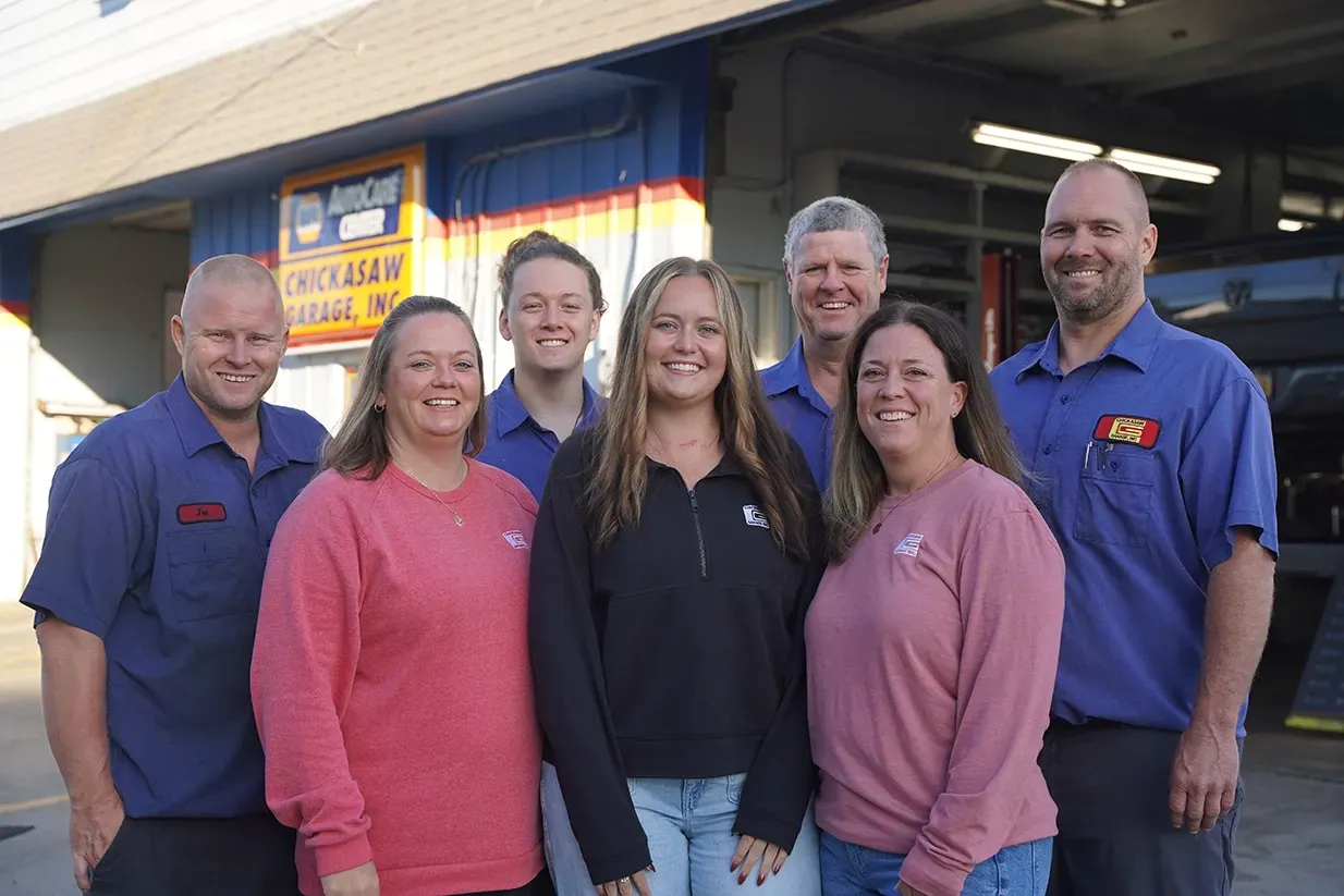 Group of seven people smiling in front of an auto repair shop.