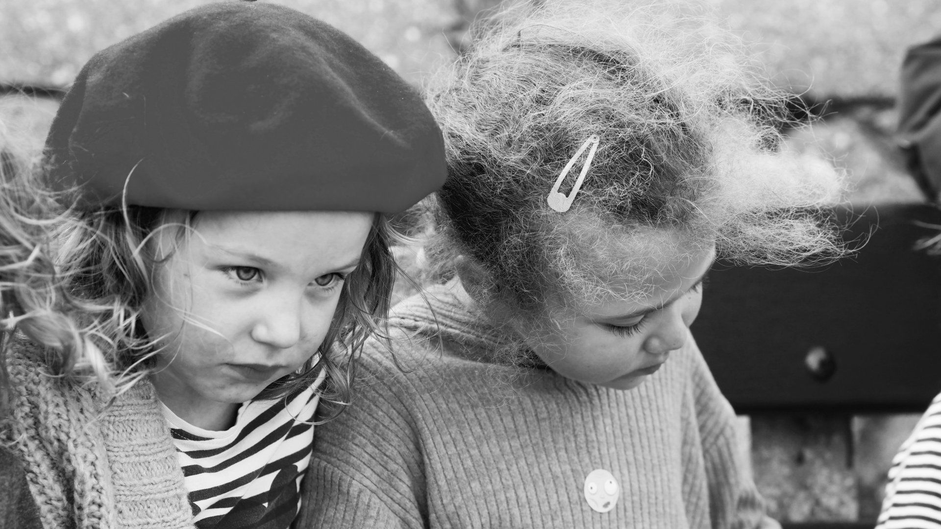 Two children sitting close together, one wearing a beret, outdoors in black and white.