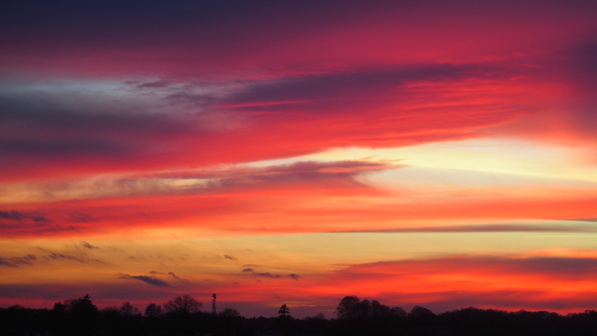 Vivid red and orange sunset over a dark tree line and distant hills