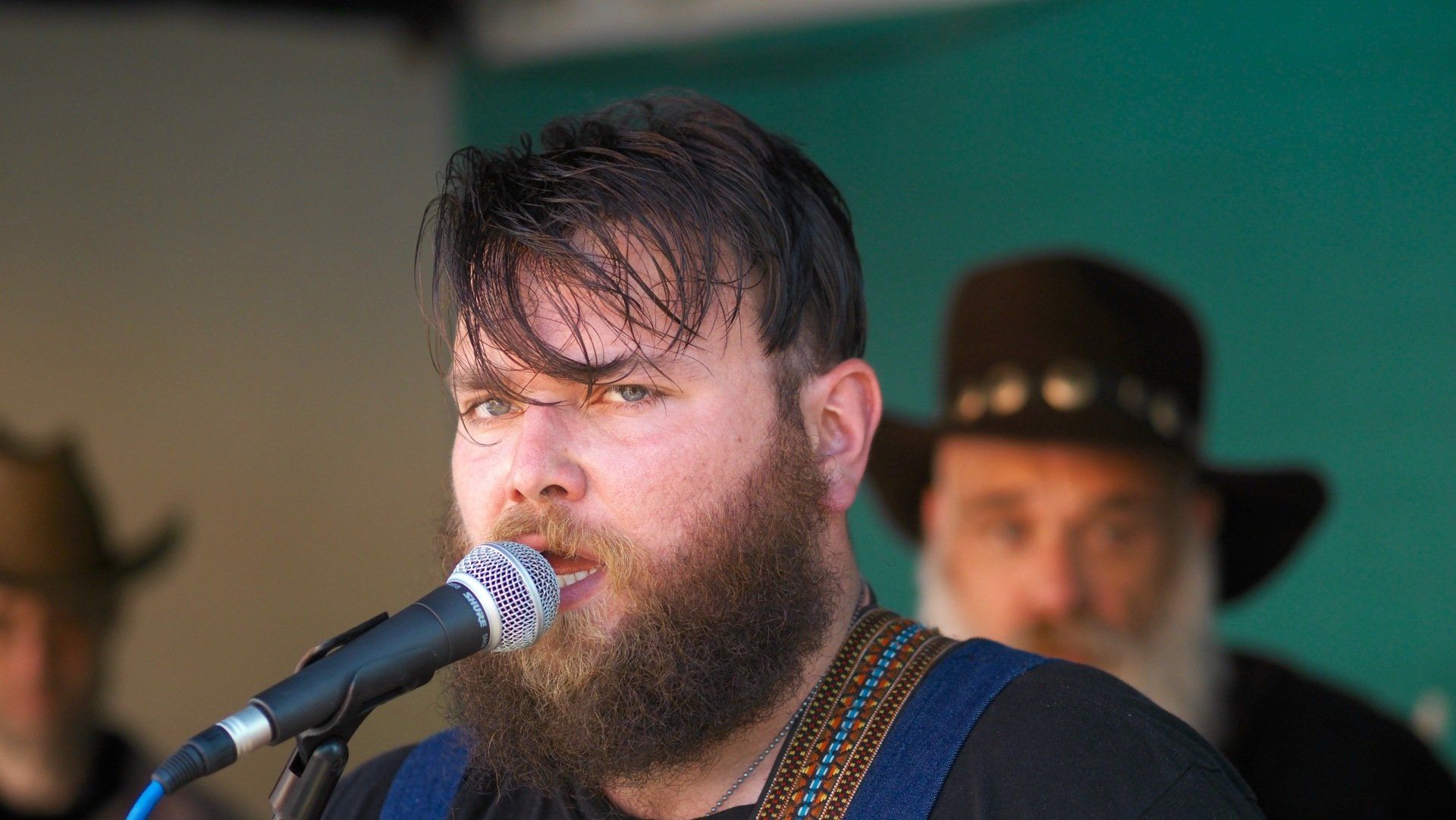 Bearded singer at a microphone onstage, with blurred musicians in the background