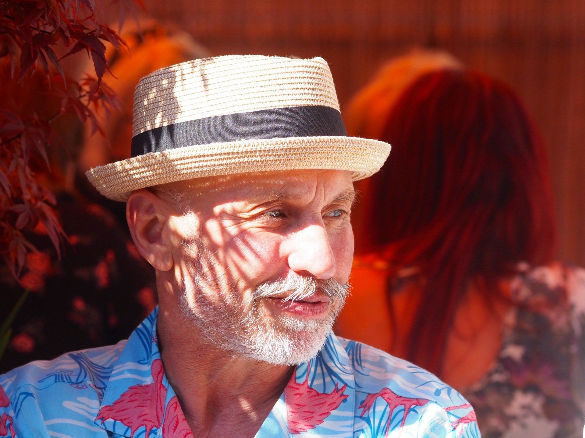 Man in straw hat and blue floral shirt looking right in warm red sunlight