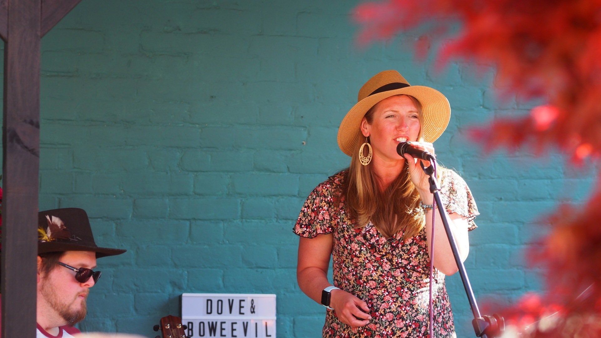 Singer in straw hat performing onstage beside a keyboard player against a teal wall.