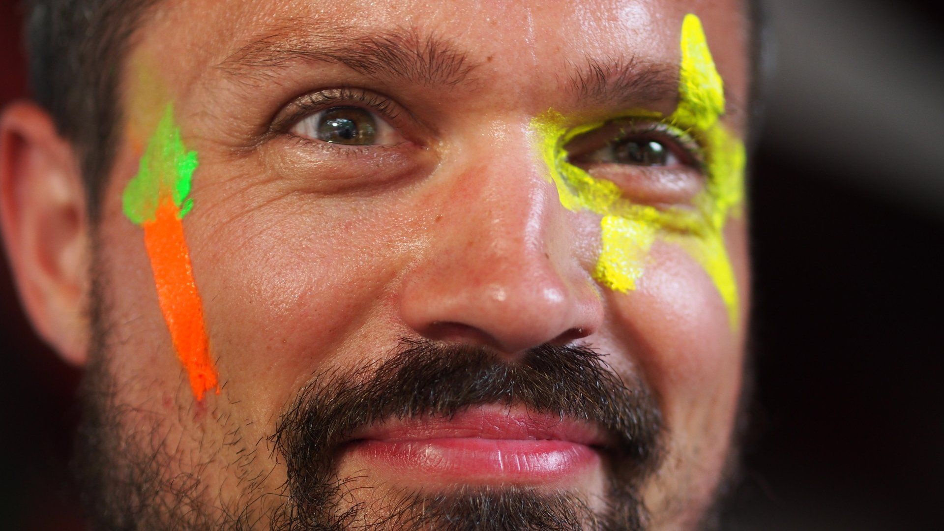 Close-up of a smiling face with bright green and orange face paint