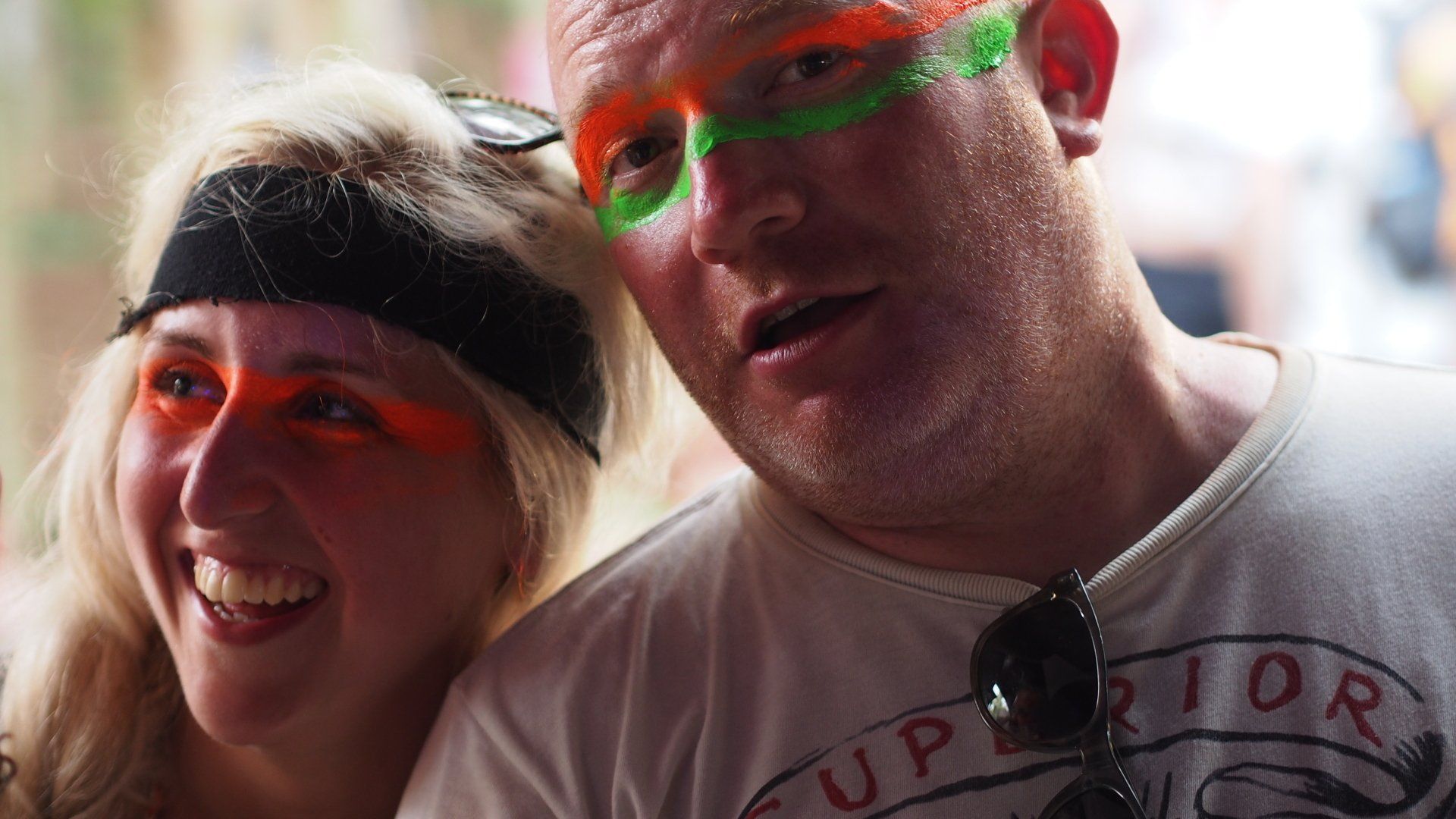 Two smiling people wearing neon face paint at an outdoor event