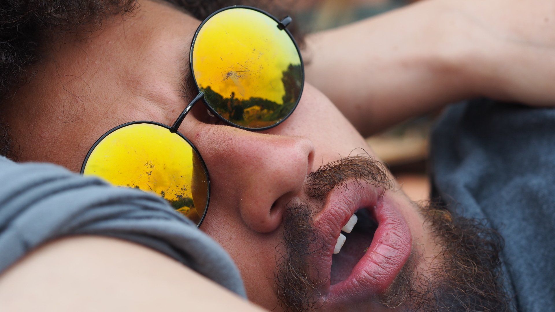 Close-up of a man wearing reflective yellow sunglasses, resting with his face turned sideways.