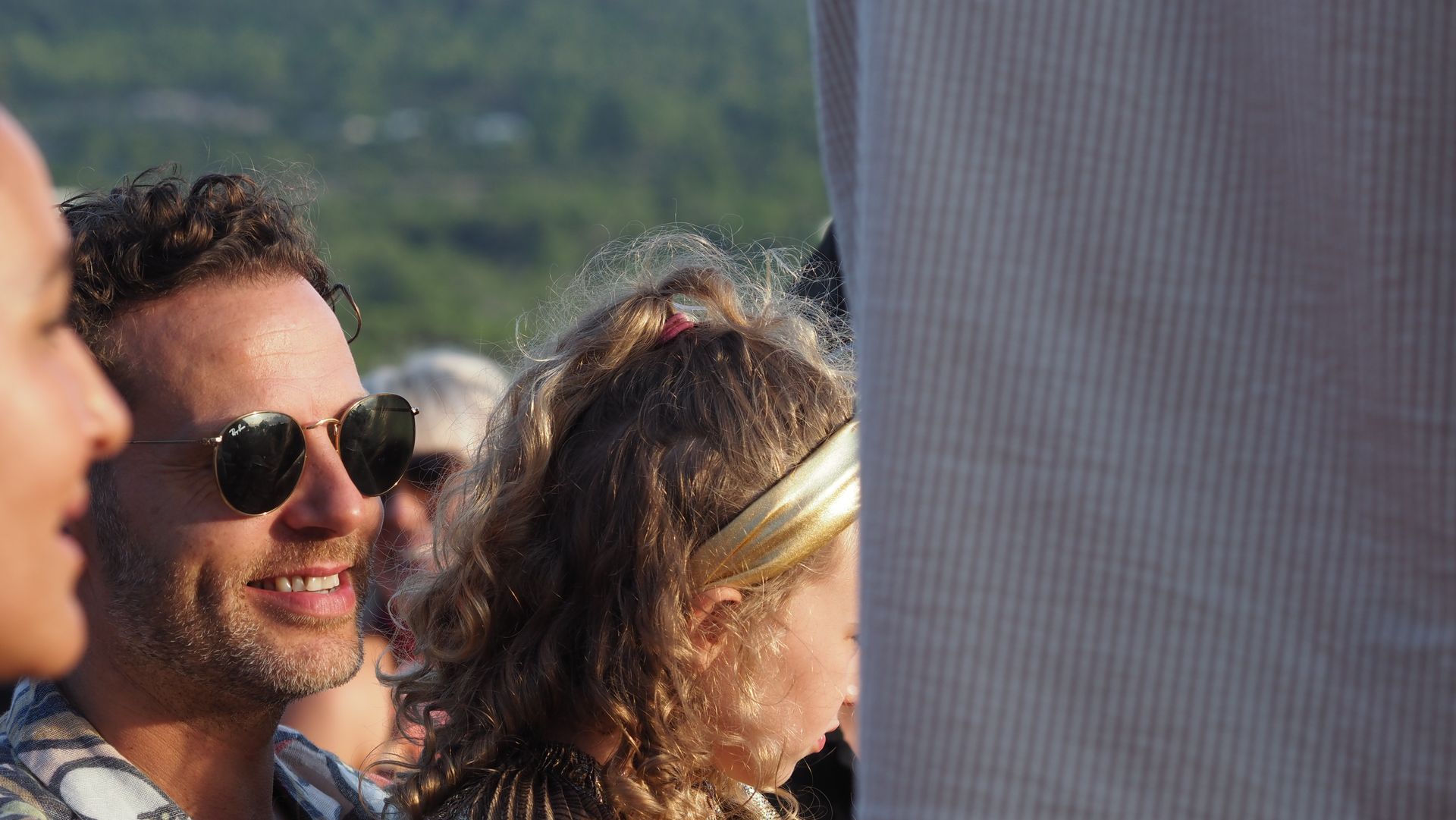 Smiling crowd outdoors, with a man in sunglasses in the foreground.