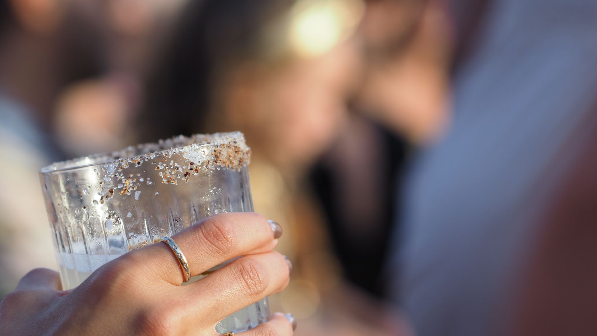 Hand holding a clear glass with condensation against a blurred outdoor background