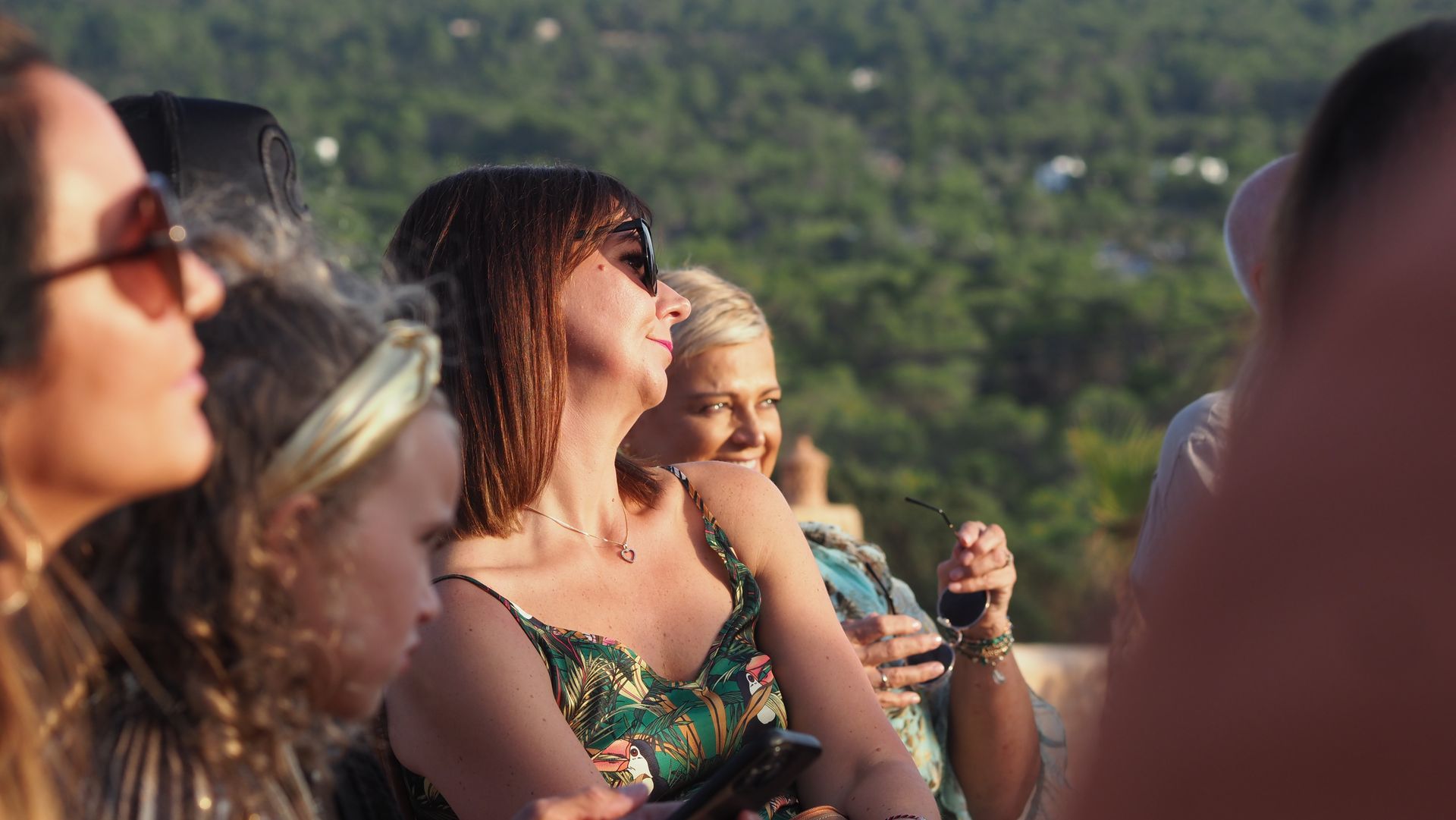 People at an outdoor concert, with a woman in sunglasses holding a drink in the foreground.