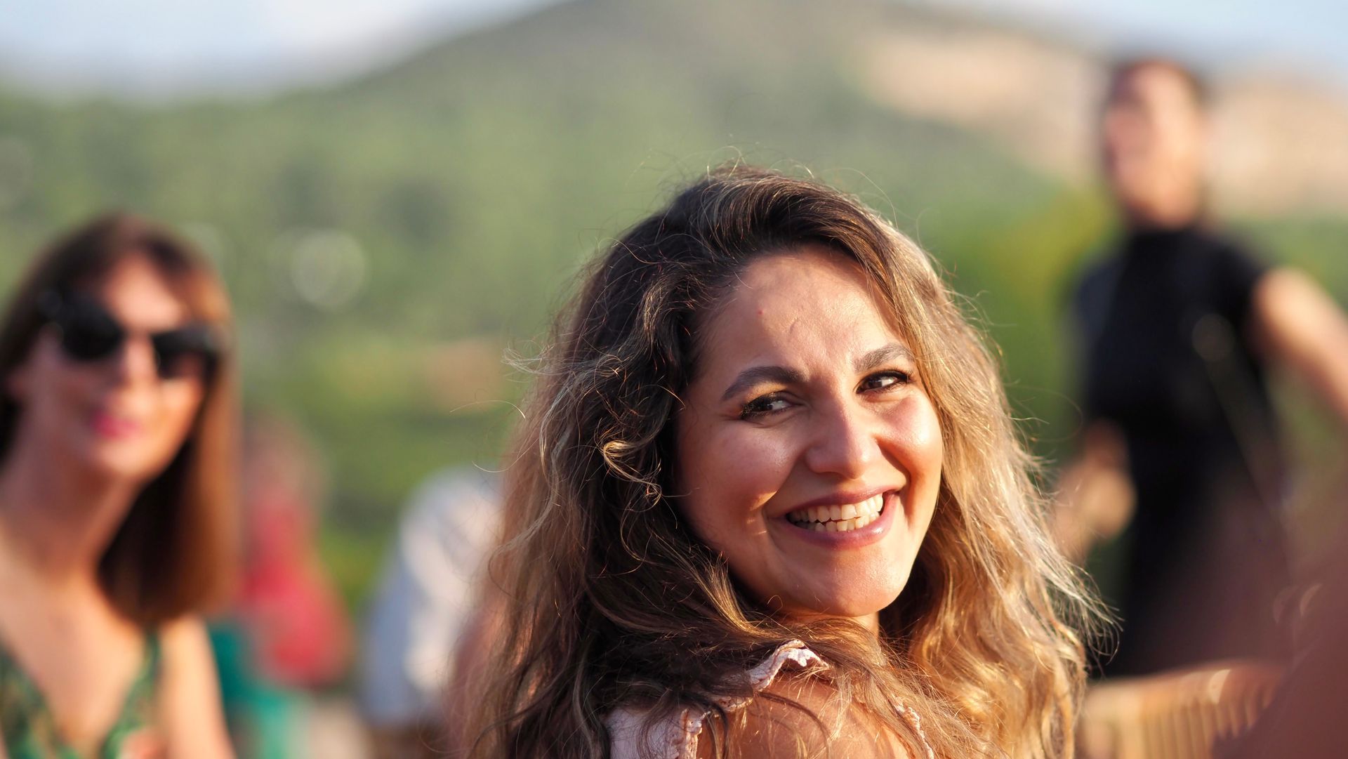 Smiling woman outdoors with blurred people and greenery in the background