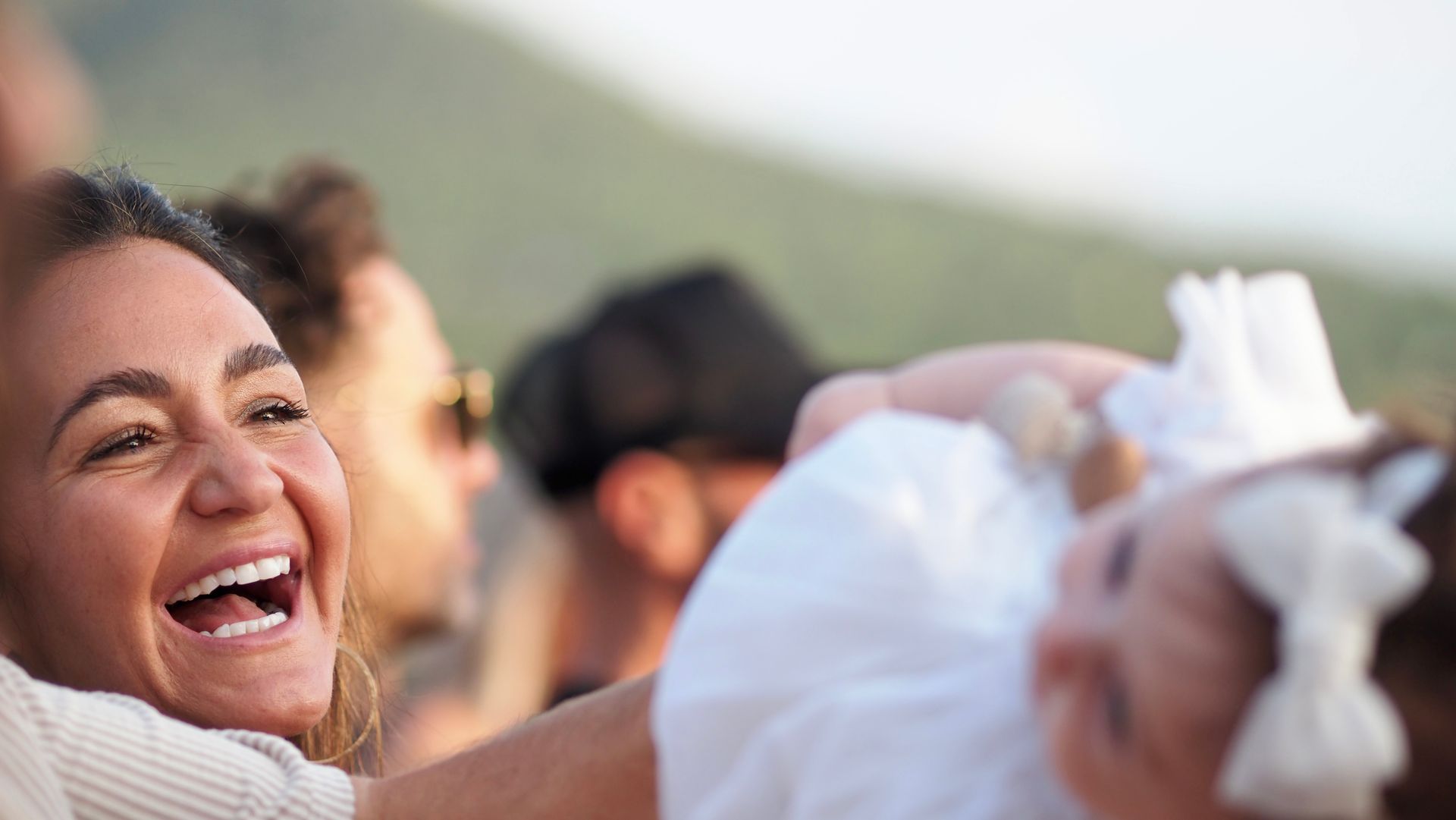 Smiling woman laughing outdoors, reaching toward a white cloth in a crowd